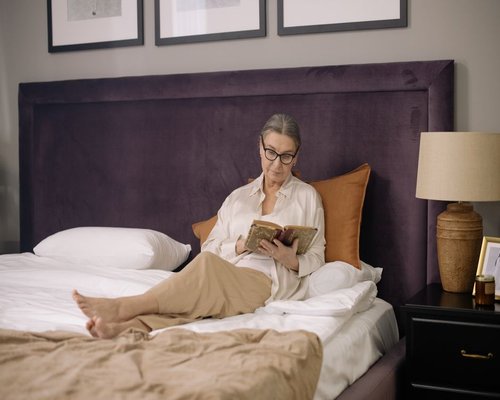 A person reading a book in bed with a warm directional reading lamp